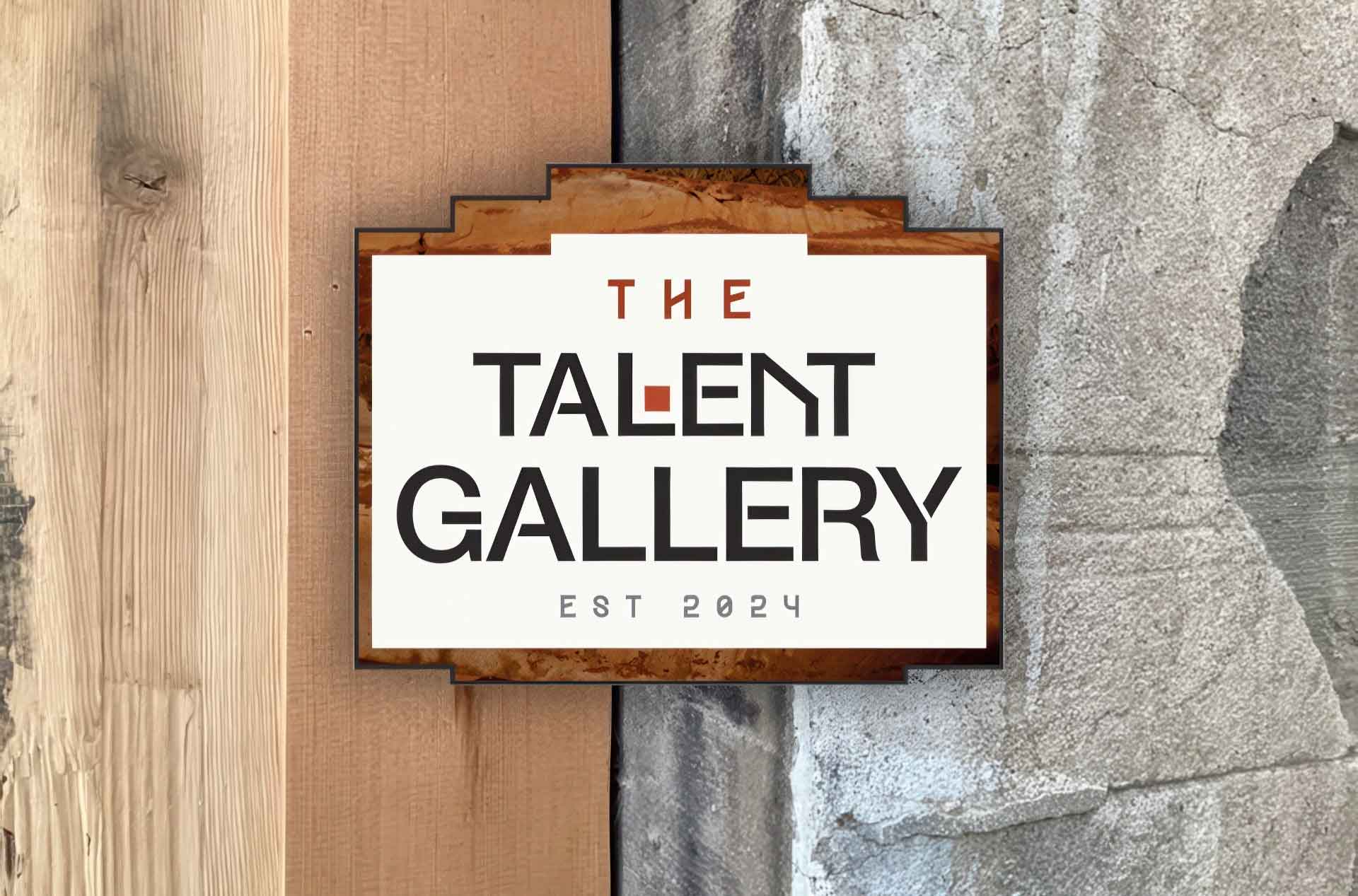 A sign reading “The Talent Gallery, Est. 2024” mounted between a wood wall and a stone wall.