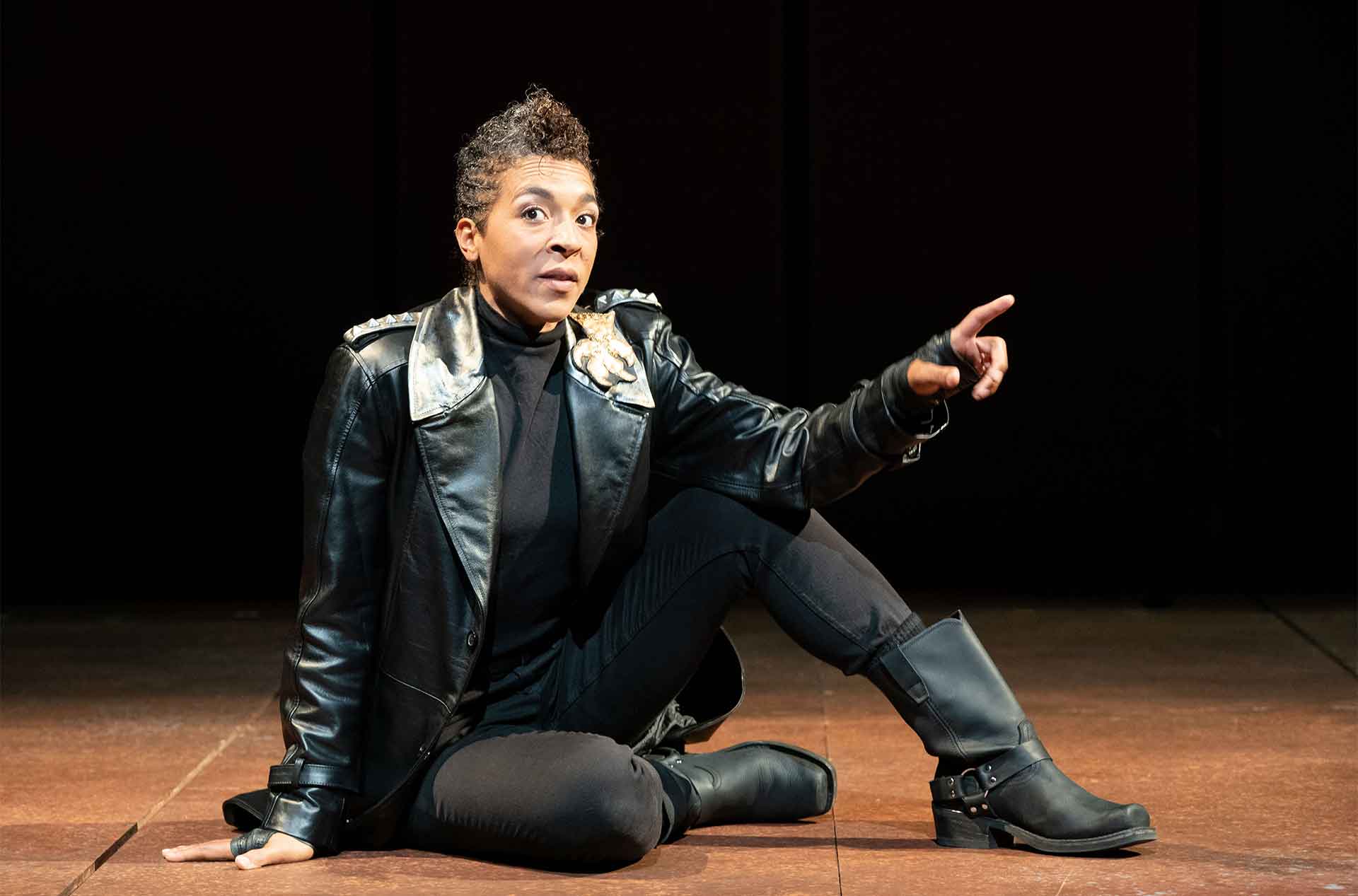 Person sitting on stage with arm on one knee.