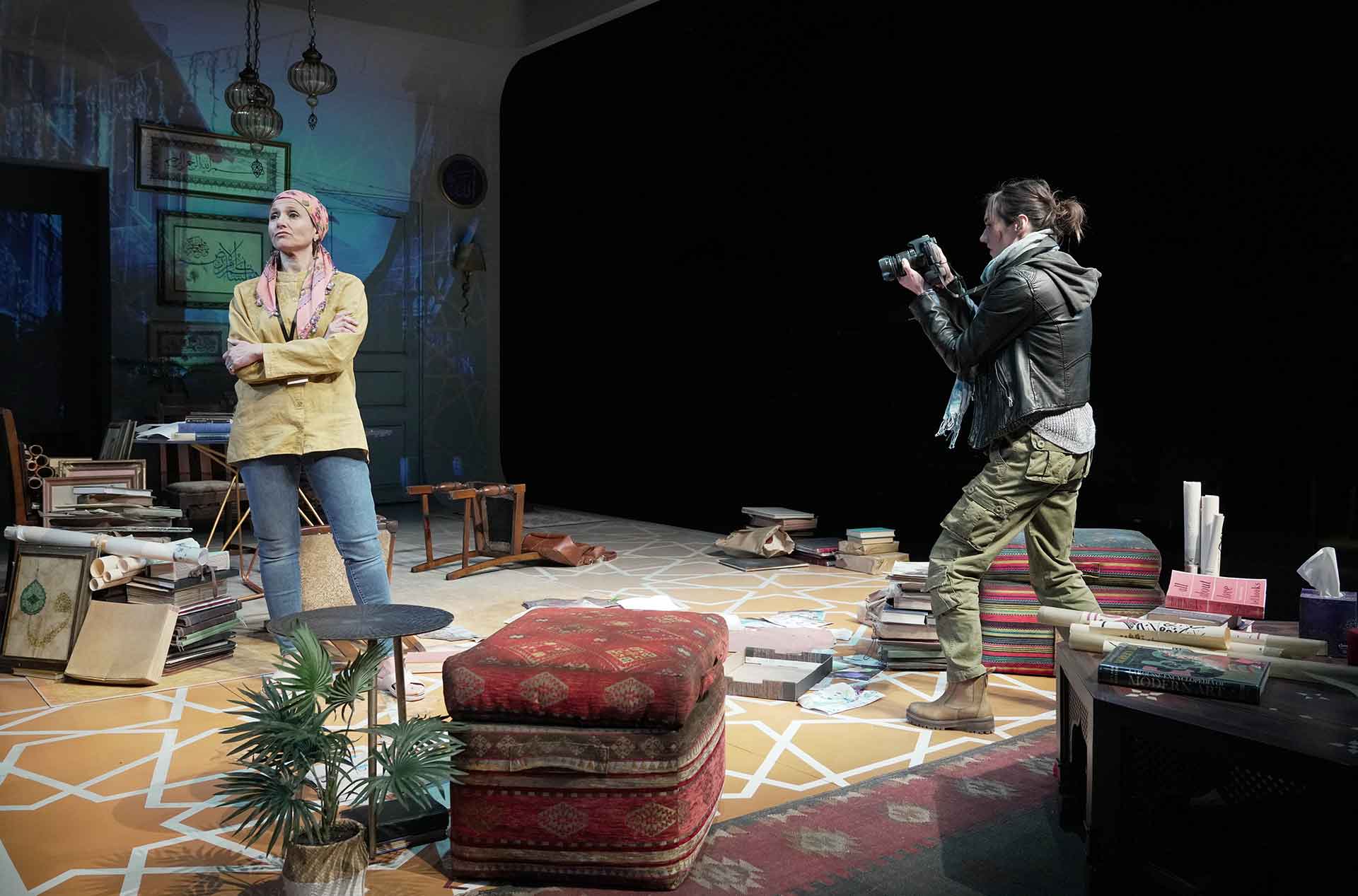 A person standing with their arms crossed while another takes a photo of them.