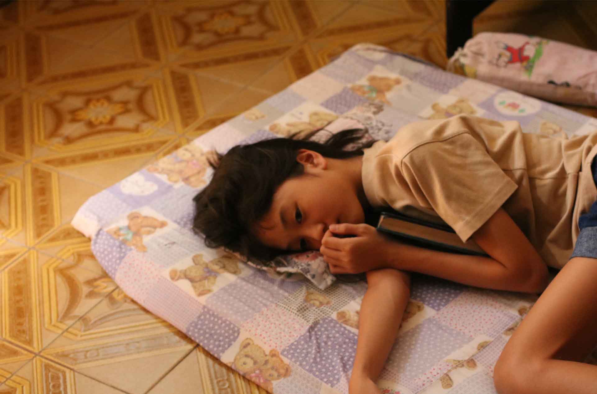 A girl laying on the floor on her side holding onto a book.