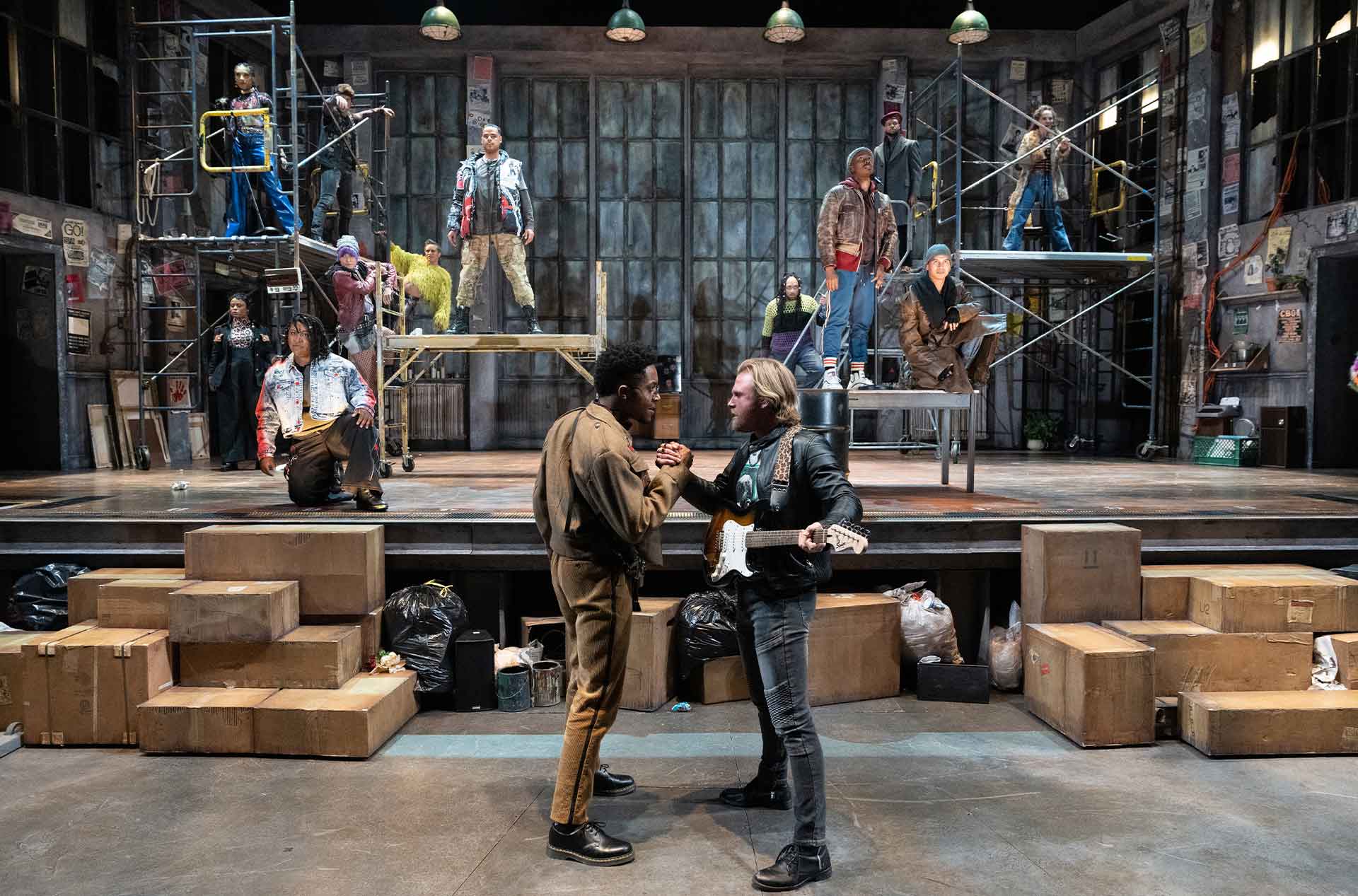 Two people gripping each other's hand in a handshake with a group of people behind them on stage.