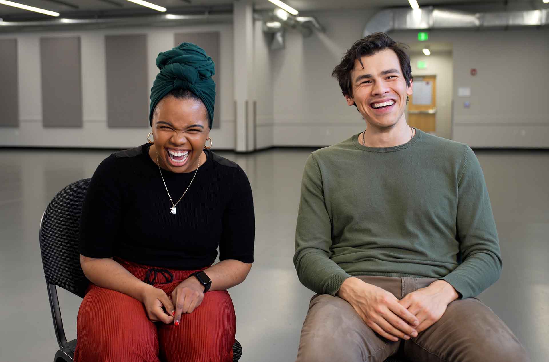 Two people sitting, looking at camera laughing and smiling during an interview.