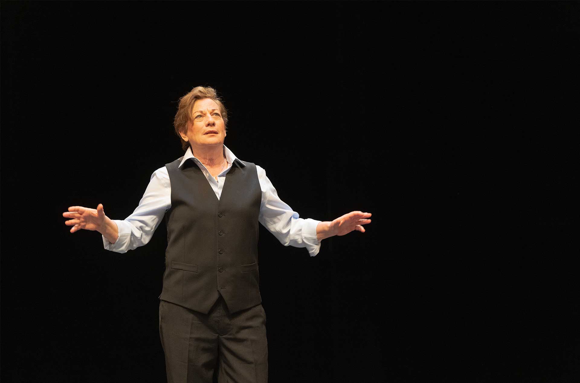 A person standing before a dark background with their arms held out in discussion.