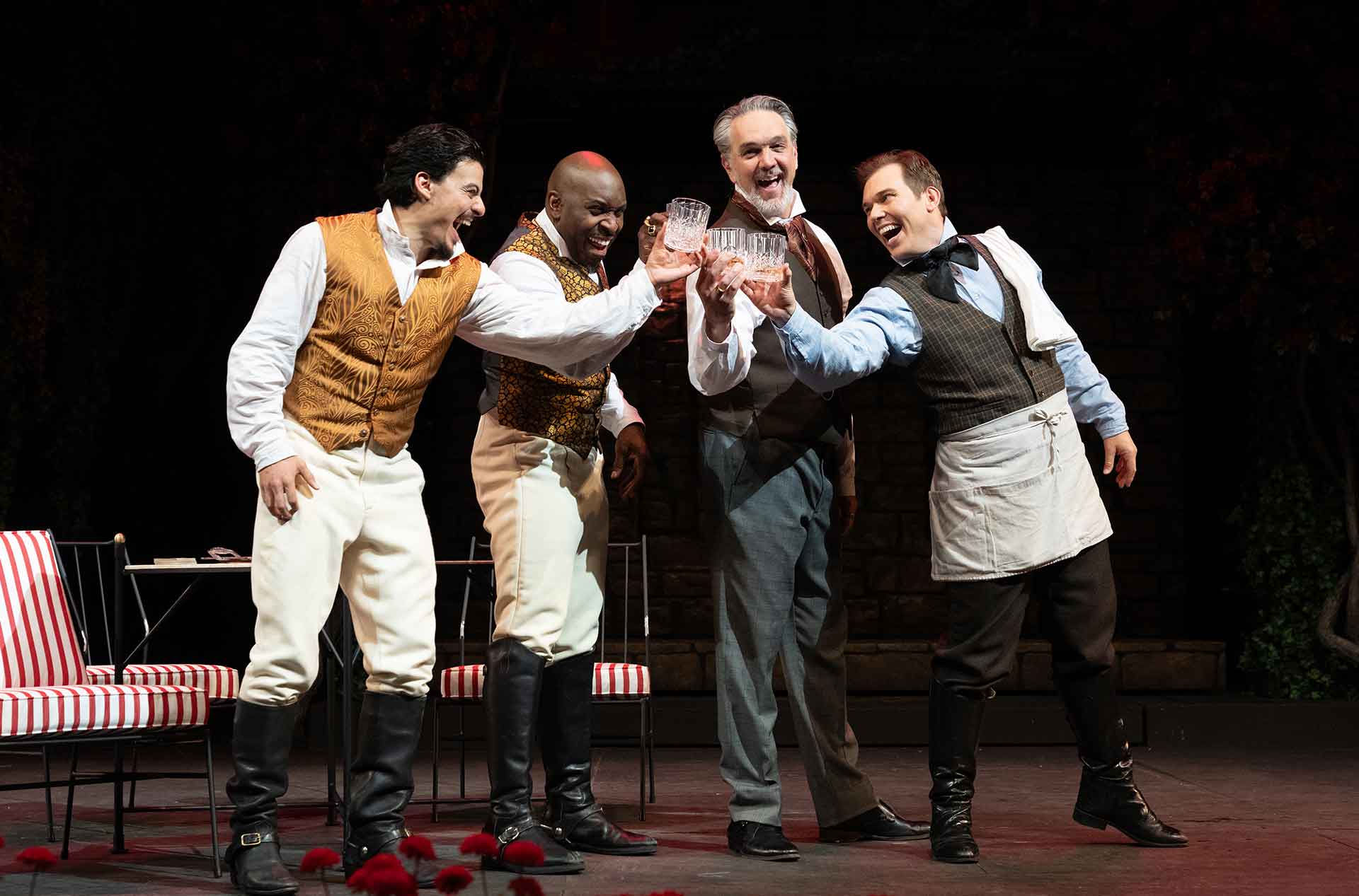 Four people standing by each other laughing and toasting with glasses.