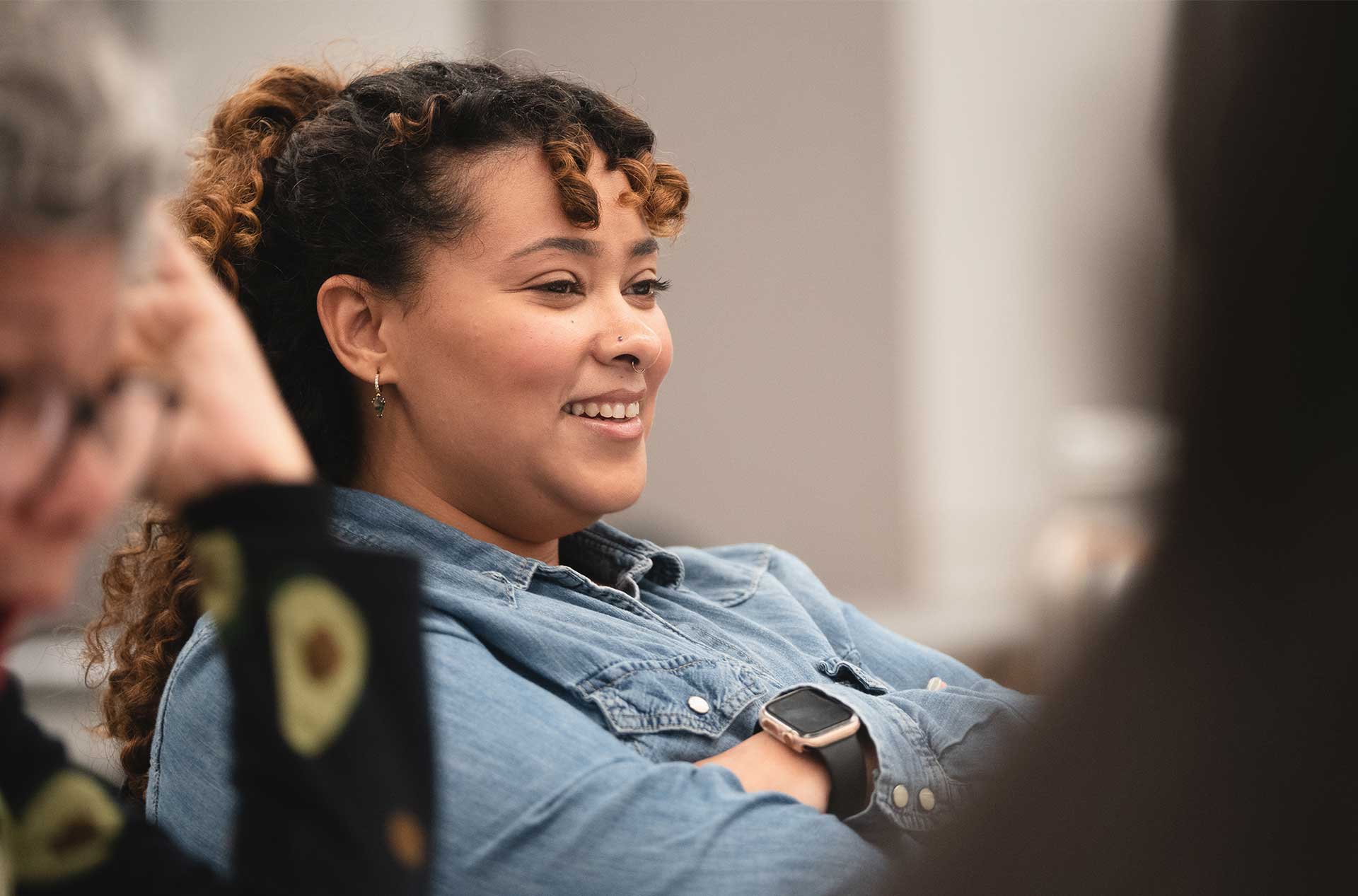 Close-up of a smiling participant in a denim shirt with arms crossed, engaged during a rehearsal session.