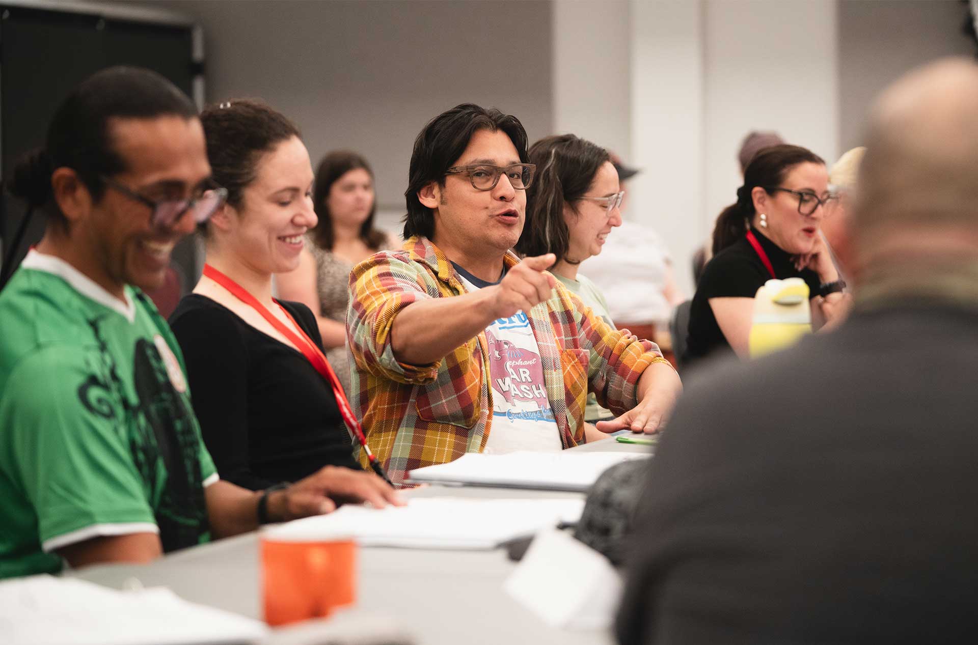 Group of rehearsal participants laughing and actively engaging around a table, with scripts and highlighters in front of them.