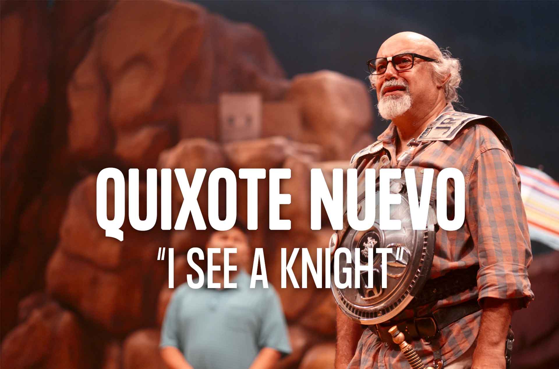 An actor, dressed in a plaid shirt and armor, stands on stage with a serious expression. The text "QUIXOTE NUEVO 'I SEE A KNIGHT'" is prominently displayed.