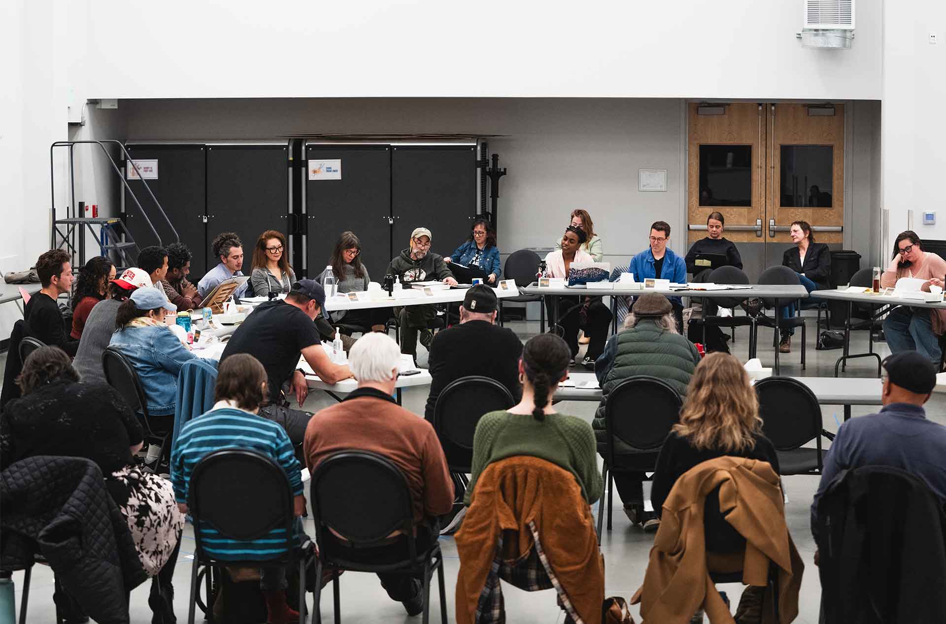 Cast and creative team seated in a large circle during a staged reading or play rehearsal.