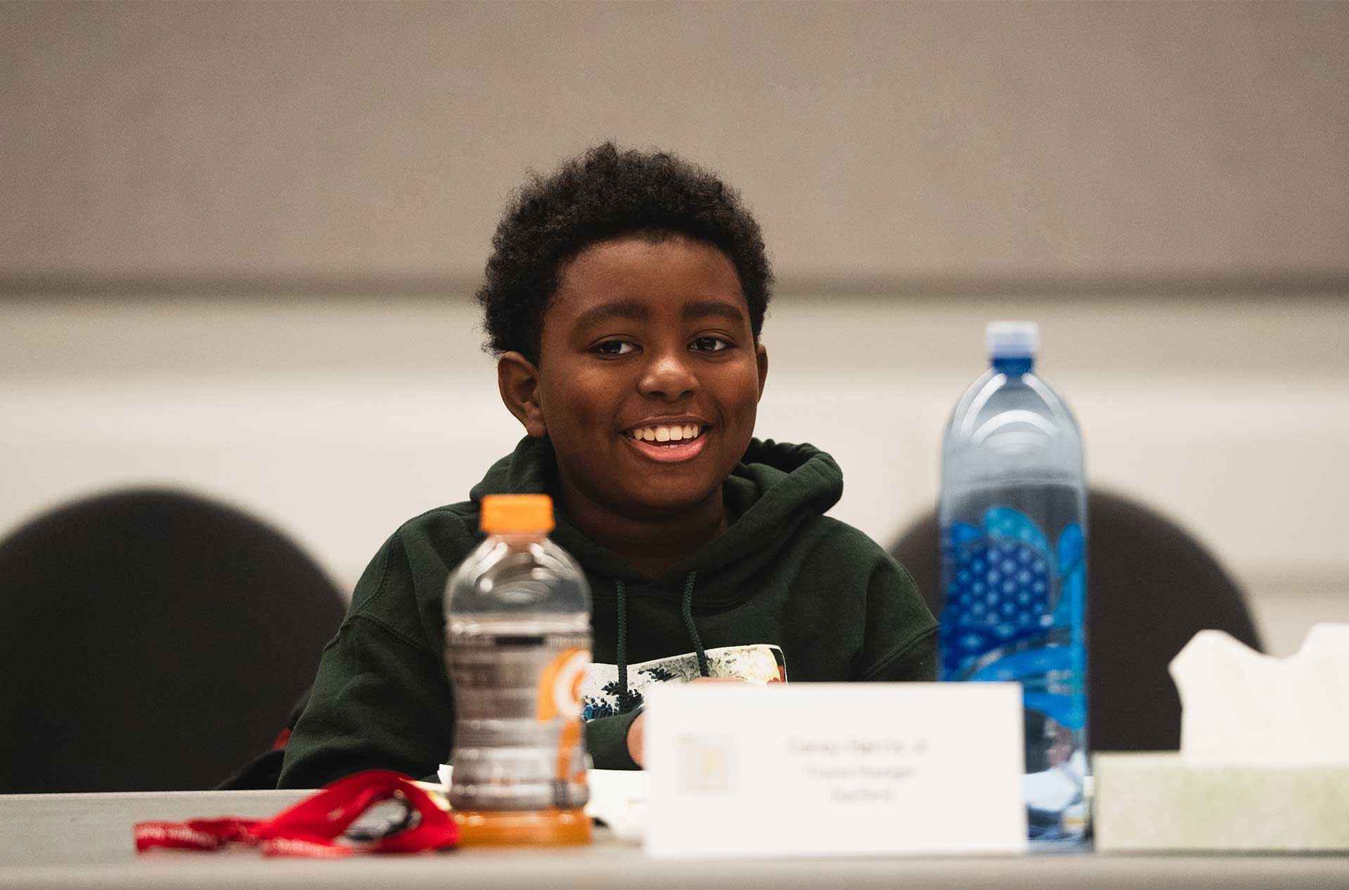 Young participant smiling at the table with drinks, papers, and a name card in front.