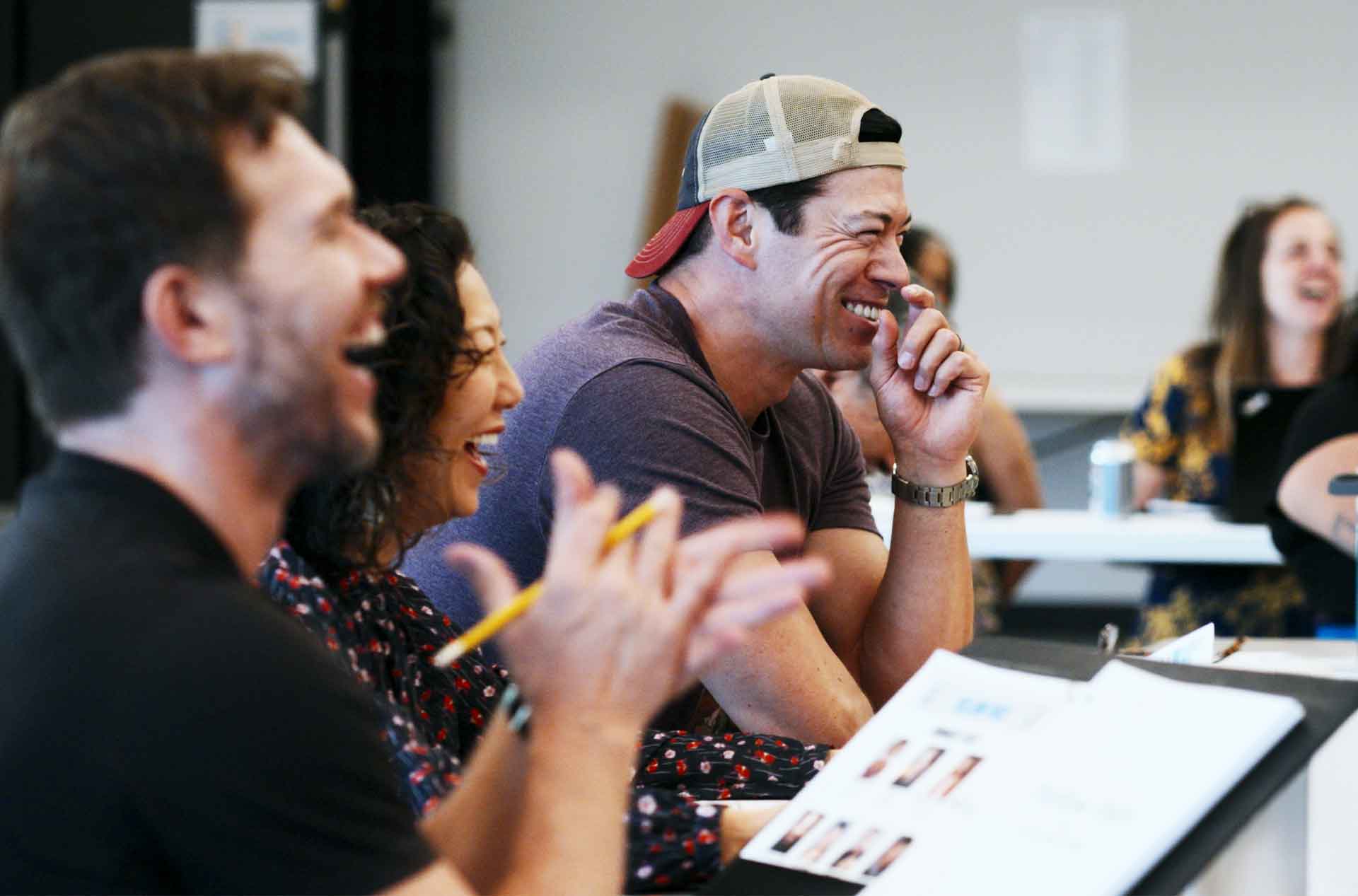 Cast members and creative team laugh together around a table during the first read through of a play.