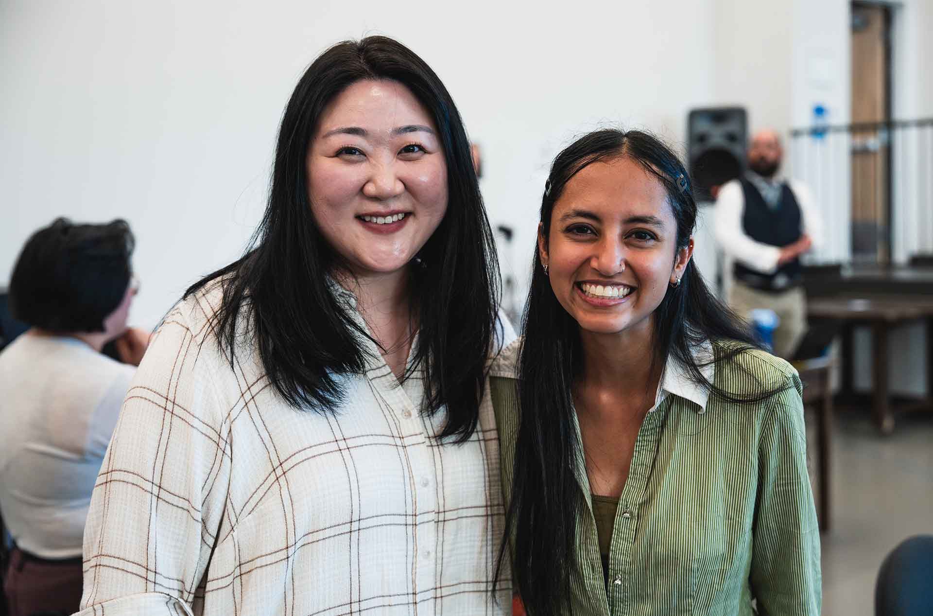 Two creative team members smile at the camera in a play rehearsal room.