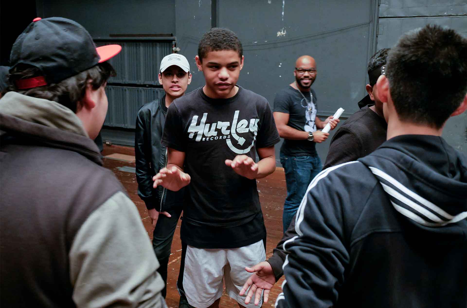 A student standing in the center of a group of students in a theater workshop.