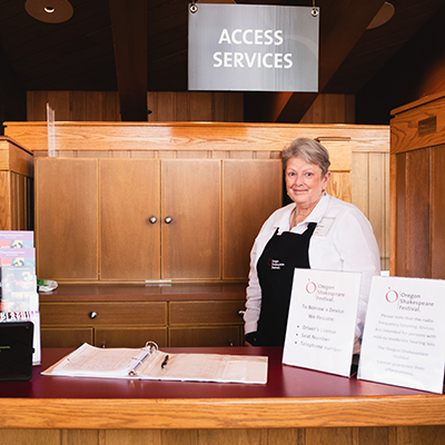 Person standing at an Access Services desk with brochures, signs, and a binder on the counter.