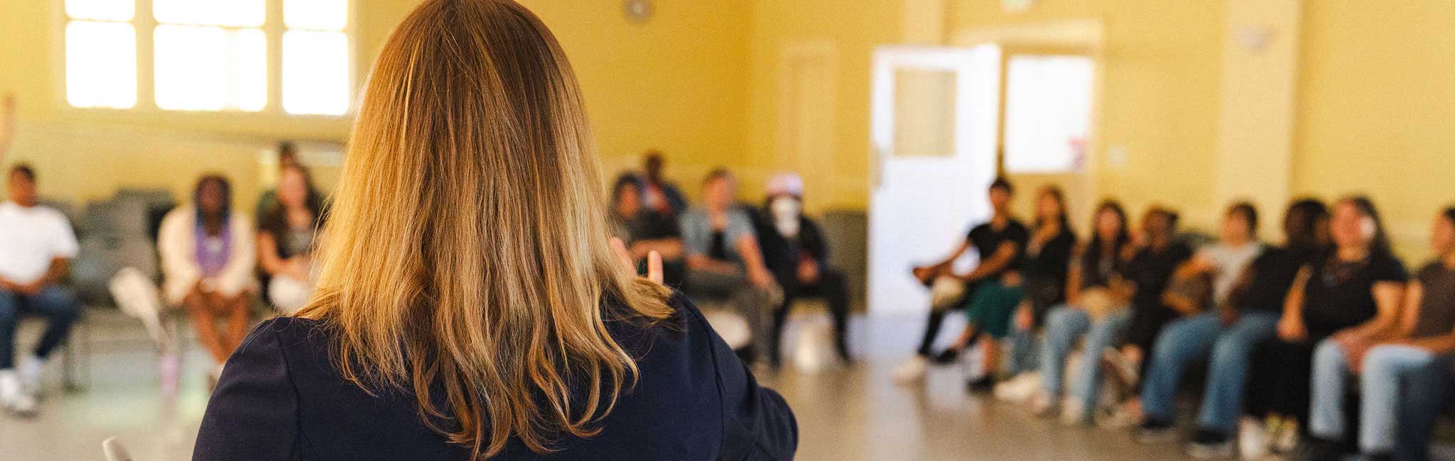 A group of people sitting in a semicircle listening to a speaker.