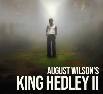 A lone figure in dark pants, white tank top, and a fedora stands between wooden fences in a foggy alley, illuminated by a narrow beam of light the title “August Wilson’s King Hedley II” in text.