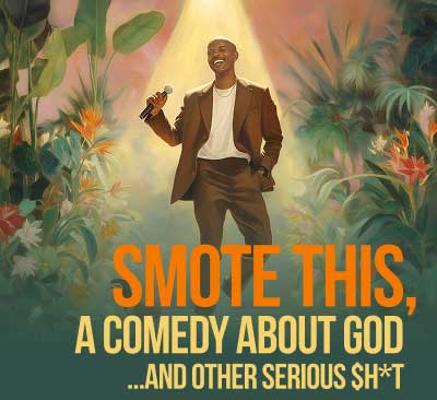 A person in a brown suit smiles while singing into a microphone under a warm spotlight, surrounded by tropical plants and bright flowers.